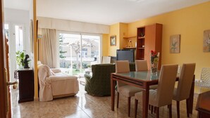 Una sala de estar con sofá, una mesa de comedor con sillas, televisor y estantería.