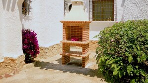 A brick oven under a white building with a window and a door, surrounded by greenery and flowers. - La Cartuja - Javea, Costa Blanca (Javea)
