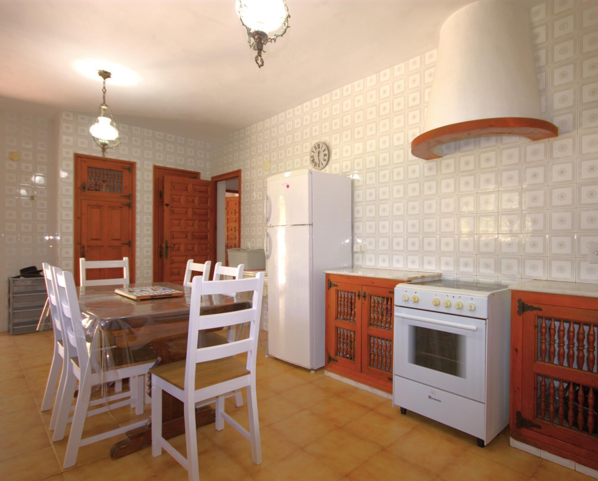 A kitchen with a dining table, chairs, a refrigerator, an oven, and a clock on the wall.