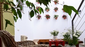 Ein Korbstuhl, eine Holzbank und ein roter Tisch mit einer weißen Blumenvase in einer Ecke.