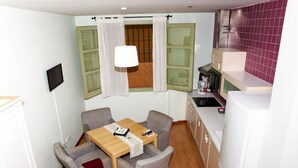 Eine kompakte Küche mit Essbereich, einem kleinen Fenster mit Vorhängen und einem an der Wand befestigten Fernseher.