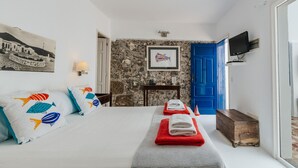 A hotel room with a bed, two pillows, a nightstand, a television, a blue door, and a stone wall. - Eufemia, Casa Rural Caleton del Golfo, El Golfo (El Golfo)