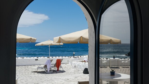 A beachside view through an arched window with white umbrellas and lounge chairs. - Eufemia, Casa Rural Caleton del Golfo, El Golfo (El Golfo)