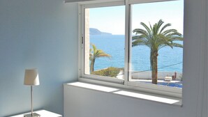 A room with a window overlooking a coastal view, including palm trees and the sea.