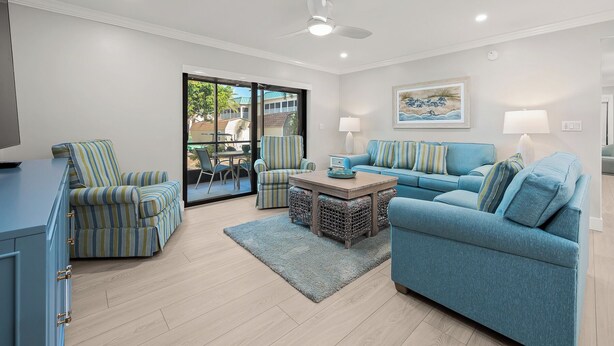 A modern living room with a blue sofa, striped armchairs, a coffee table, and a dining area with a table and chairs. - Newly Renovated Garden View 2 bed, 2 bath at Sanibel Moorings #1131 (Sanibel)