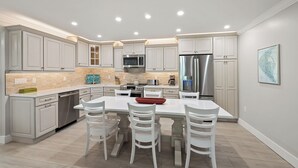 A modern kitchen with white cabinetry, a central island with chairs, stainless steel appliances, and a tiled backsplash. - Newly Renovated Garden View 2 bed, 2 bath at Sanibel Moorings #1131 (Sanibel)