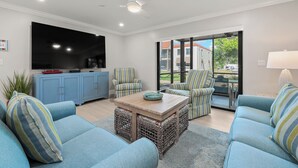 A modern living room with a flat-screen TV, blue sofas, striped armchairs, a wooden coffee table, and a ceiling fan. - Newly Renovated Garden View 2 bed, 2 bath at Sanibel Moorings #1131 (Sanibel)