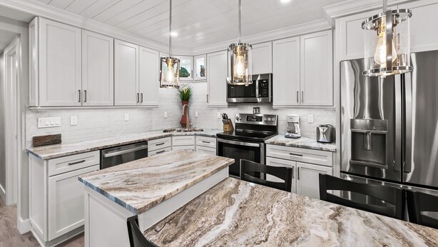 A modern kitchen with white cabinetry, a marble countertop, stainless steel appliances, and pendant lighting.