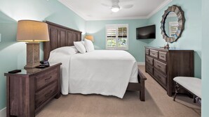A bedroom with a bed, bedside tables, a bench, a dresser, a television, and a ceiling fan.