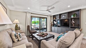A spacious living room with a large window, a ceiling fan, and a TV on a dark cabinet.