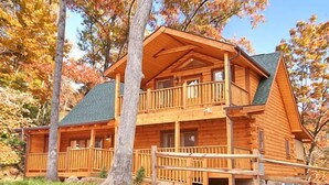 Une cabane en rondins à deux étages, dotée d’un balcon et entourée d’arbres.
