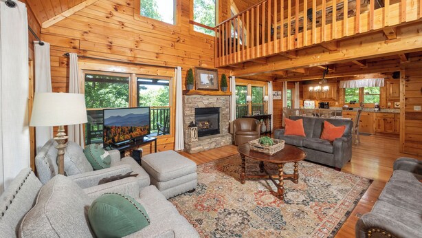 L’intérieur d’une cabane en rondins comprend une cheminée, deux canapés, une table basse et un coin cuisine.