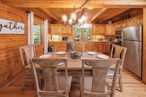 Una cucina in stile baita con tavolo da pranzo per quattro persone, frigorifero e lampadario.