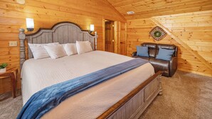 Une pièce aux murs lambrissés, avec un grand lit, un canapé en cuir et un ventilateur de plafond.