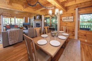 Interno di una baita in legno con un tavolo da pranzo imbandito per quattro persone, un camino e vista sull'esterno.