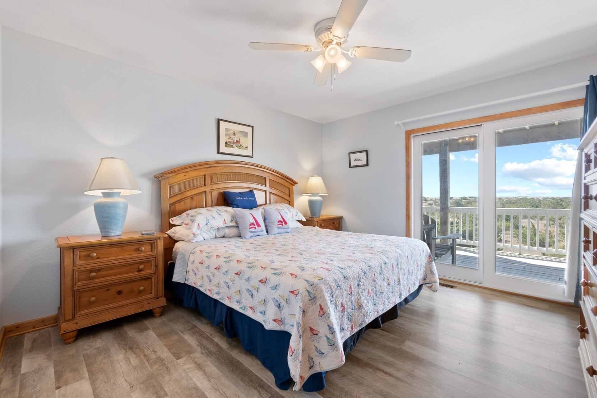 Une chambre à coucher comprenant un lit, deux tables de chevet, un ventilateur de plafond et un balcon avec vue.