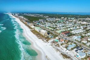 Vista aérea de un pueblo costero con una playa de arena extensa, edificios residenciales y una vista despejada del océano.