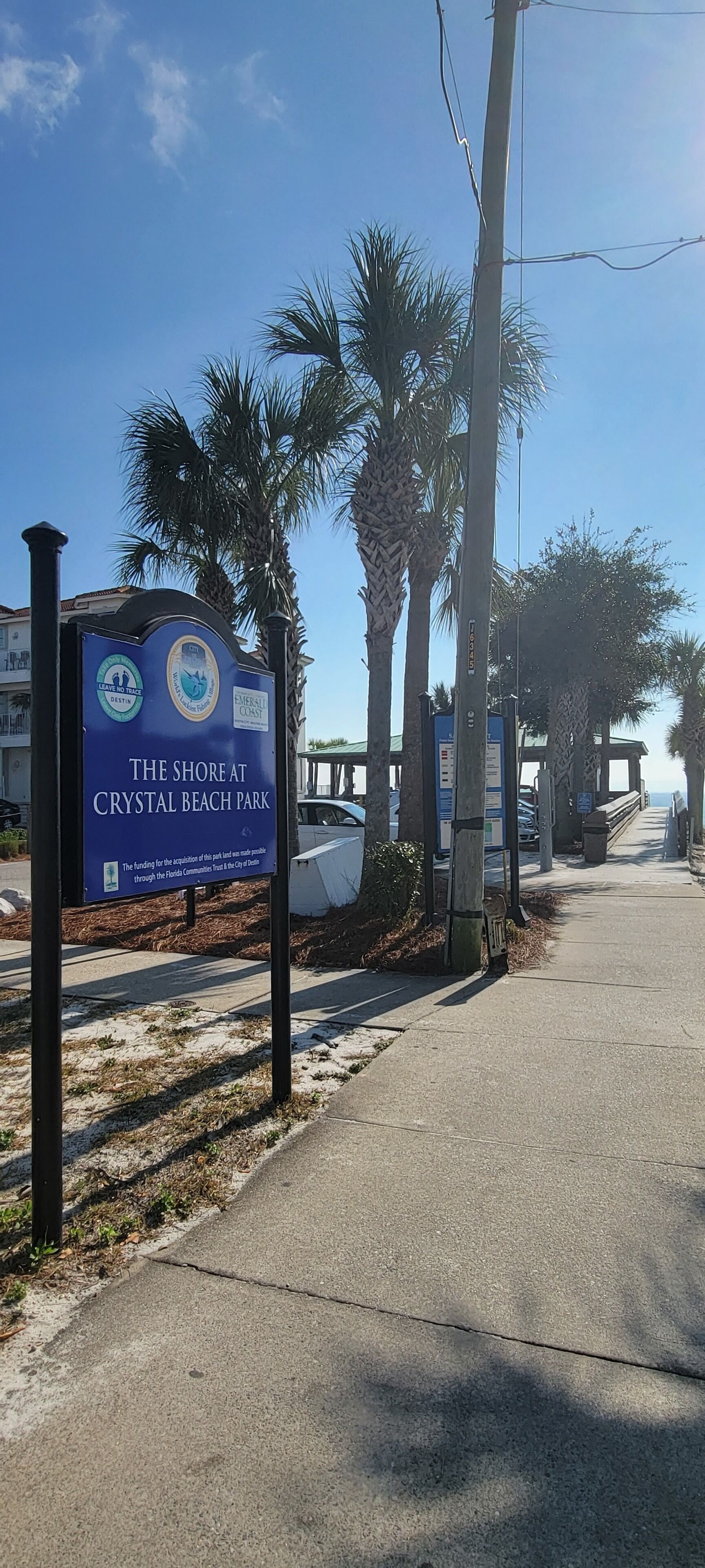 Une enseigne indiquant l’entrée du parc Crystal Beach, avec des palmiers et un ciel dégagé.