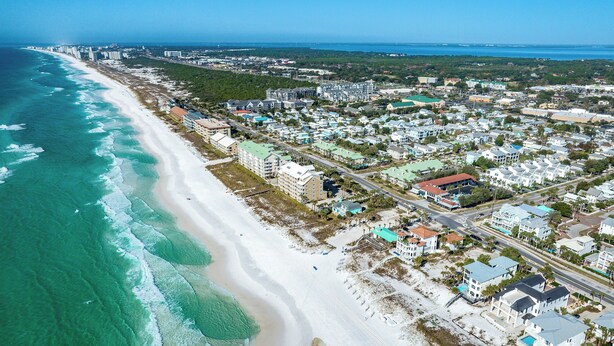 An aerial view of a coastal town with a wide sandy beach, residential buildings, and a clear view of the ocean. - 2 Queen Beds. Don`t Leave Your Dog at Home! (Destin)