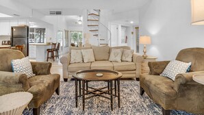 A spacious living room with a beige sofa, two armchairs, and a coffee table. A kitchen is visible in the background with white cabinets and a wooden countertop. - 2 BR with a Loft and Beach Service in Private Resort Community (Miramar Beach)
