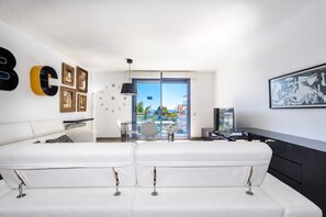 En moderne stue med sofa, spisebord og tv. Væggen er dekoreret med billeder, og et stort vindue giver udsigt.