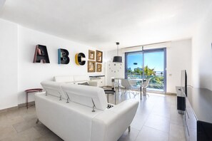 Een moderne woonkamer met een witte bank, een eethoek met een tafel en stoelen, een televisie, en een balkon met uitzicht.