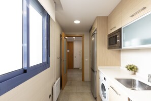Een kleine keuken met een ingebouwde magnetron, een wasmachine en een spoelbak.