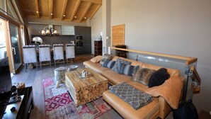 A spacious living area with a leather sofa, a wooden coffee table, and a dining table with chairs. A kitchen is visible in the background.