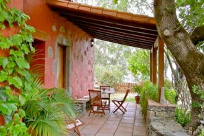 Une terrasse avec une table et des chaises, entourée de verdure et d’un mur en pierre.