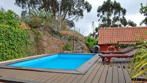 A swimming pool with a wooden deck, surrounded by greenery and a red-roofed building. - Enchanting 2-Bedroom Canarian House with Private Pool in Fontanales, M (Carretera Moya Palmital)