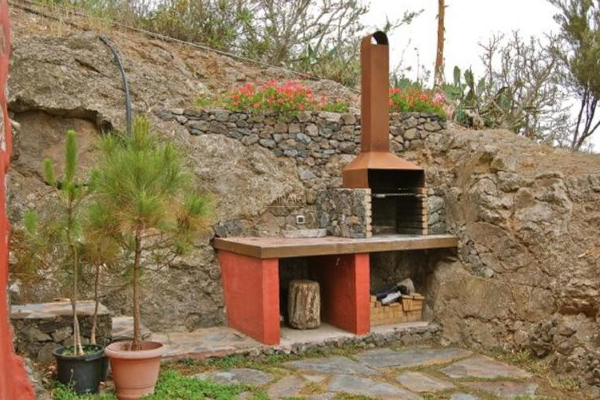 A stone-built outdoor kitchen with a chimney, potted plants, and a stone wall.