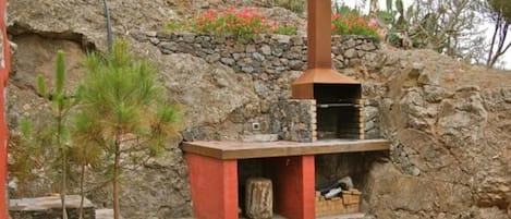Cocina exterior de piedra con chimenea, plantas en macetas y un muro de piedra.