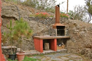 A stone-built outdoor kitchen with a chimney, potted plants, and a stone wall. - Enchanting 2-Bedroom Canarian House with Private Pool in Fontanales, M (Carretera Moya Palmital)
