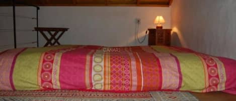 A bedroom with a bed, a wooden ceiling, a wall-mounted lamp, and a small table.