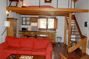 A loft-style room with a wooden staircase, a red sofa, a kitchen area, and a window.