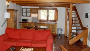 Een loft-achtige kamer met een houten trap, een rode bank, een keukenhoek en een raam.