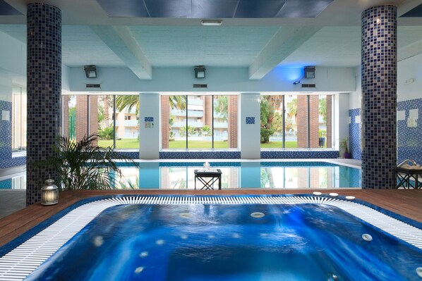 A swimming pool with a hot tub, surrounded by tiled walls and large windows.