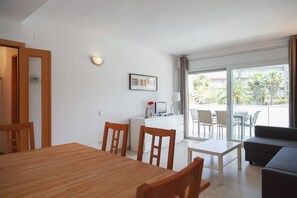 A modern living room with a wooden dining table, a sofa, and a balcony with a view of palm trees.