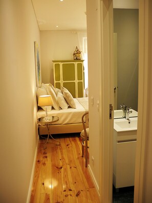 Une chambre à coucher de taille réduite, comprenant un lit, une table de chevet, une lampe et donnant sur une salle de bain avec un lavabo.
