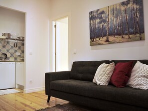 Un salon avec un canapé gris foncé, des coussins à motifs et un tableau représentant une forêt.