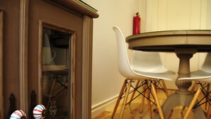 A wooden cabinet with glass doors, a white chair, and a round table with a red object on the wall. - Refurbished apartment with air conditioning in the center of Setúbal (Setúbal)