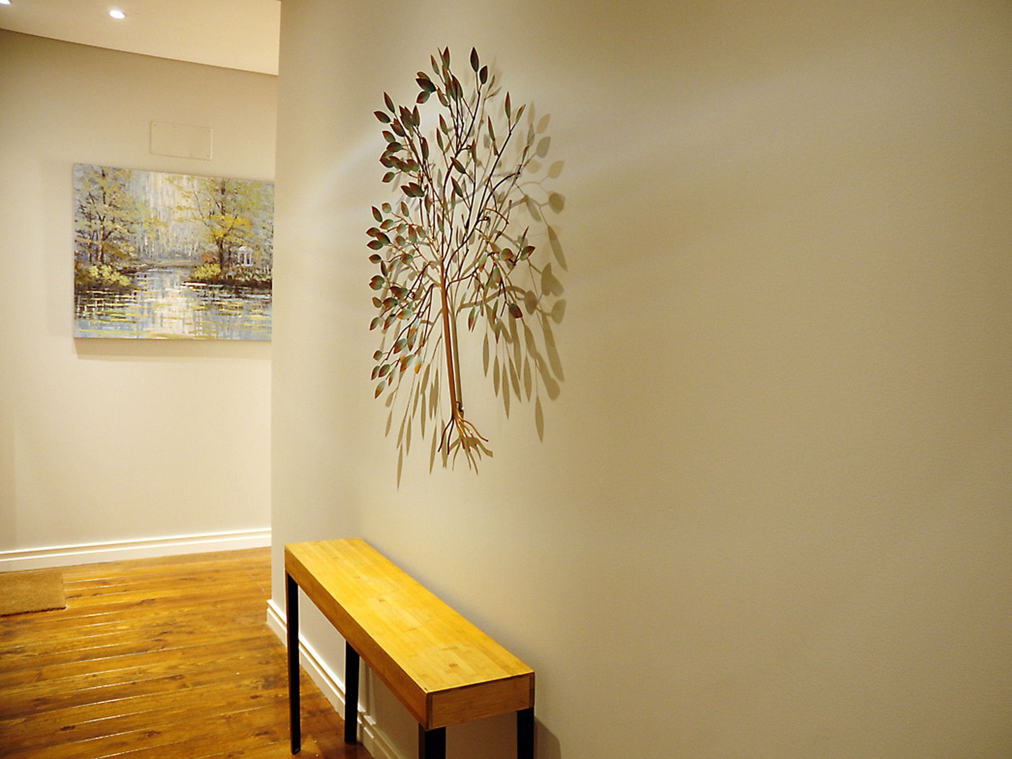A room with a wooden bench, a wall-mounted tree sculpture, and a painting of a landscape.