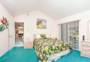 Une chambre à coucher avec un lit, une porte donnant sur un coin repas, une fenêtre avec des stores et un tableau accroché au mur.