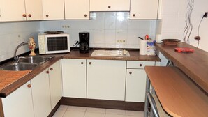 A compact kitchen with white cabinets, a microwave, a coffee maker, and a small table with stools.