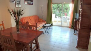 A living room with a sofa, dining table, chairs, a clock, and a view to an outdoor balcony.