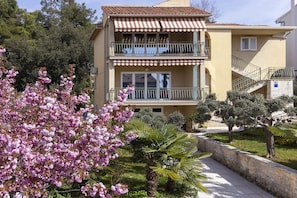 Un immeuble à plusieurs étages doté de balcons, d’un chemin pavé de pierres et d’un arbre en fleurs.