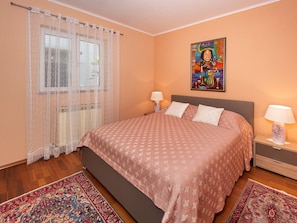 Une chambre à coucher avec un lit, deux tables de chevet, une commode, une fenêtre avec des rideaux et un tableau au mur.