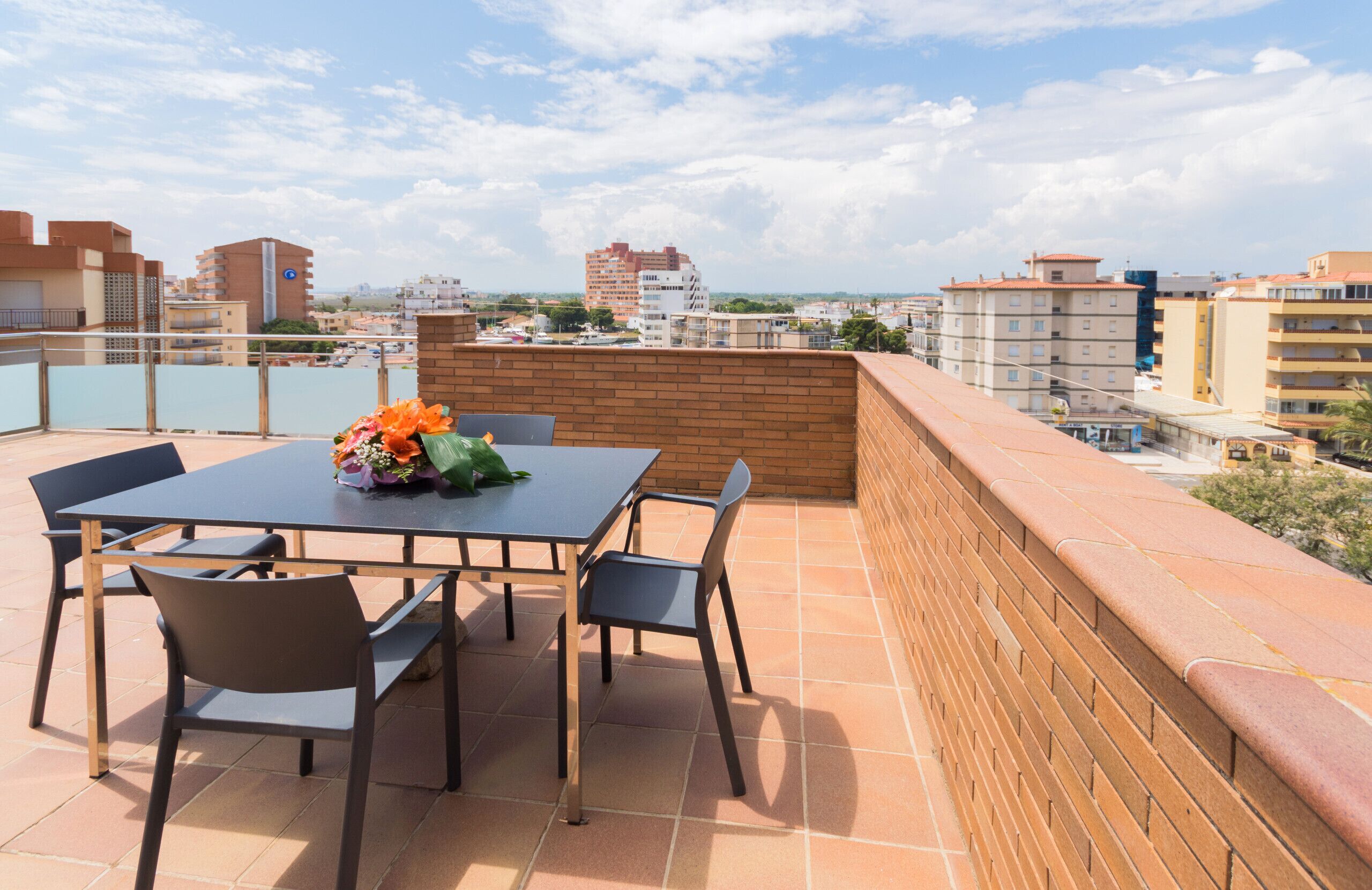 A rooftop terrace with a table and chairs, a brick wall, and a view of the cityscape.