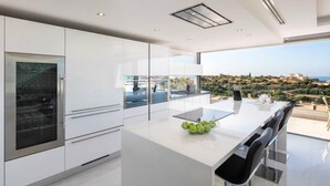 A modern kitchen with a large island, white cabinetry, and a view of a coastal landscape.