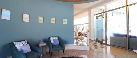A lobby with two teal armchairs, a patterned floor, and framed artwork on the wall.